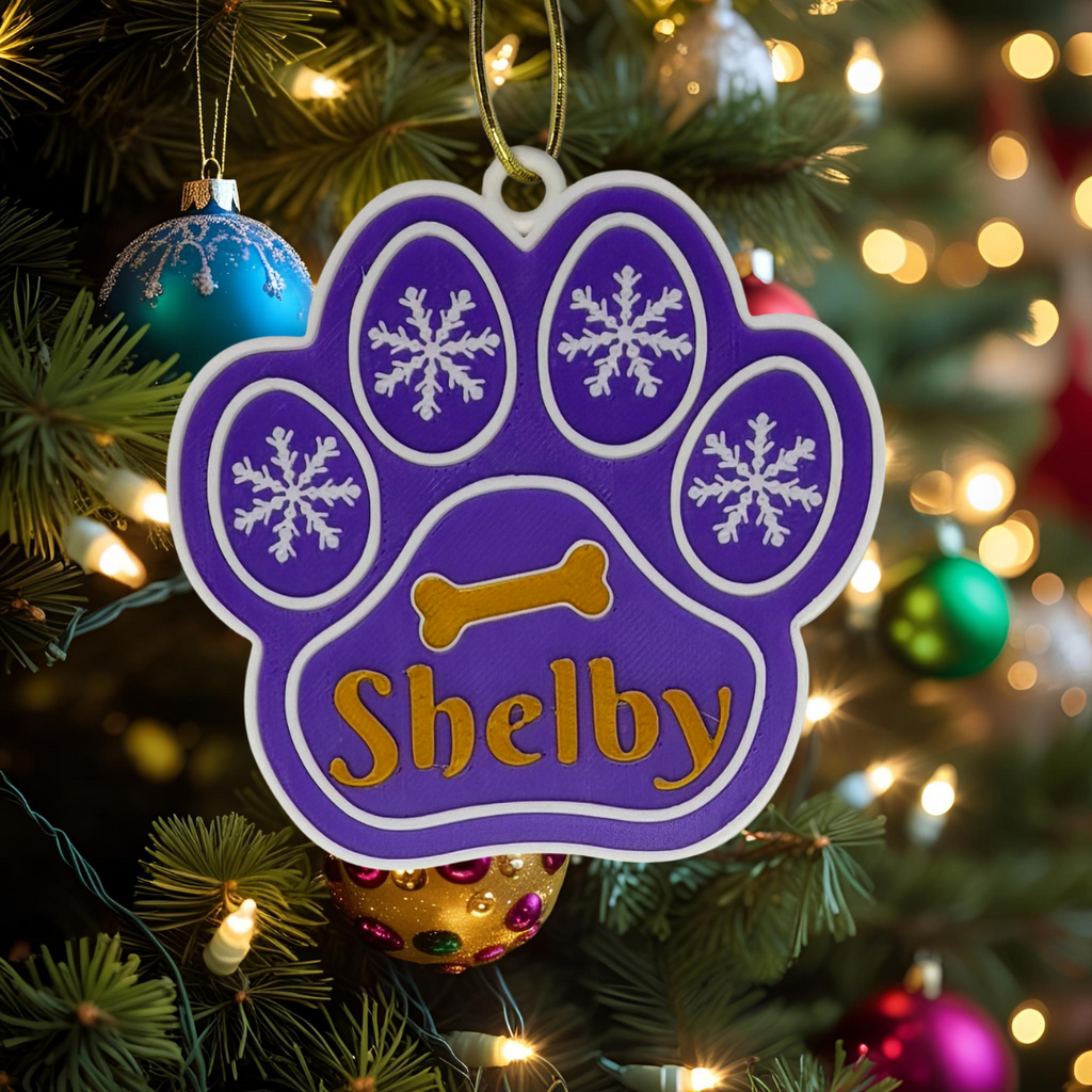 Purple paw-shaped ornament with 'Shelby' on a Christmas tree
